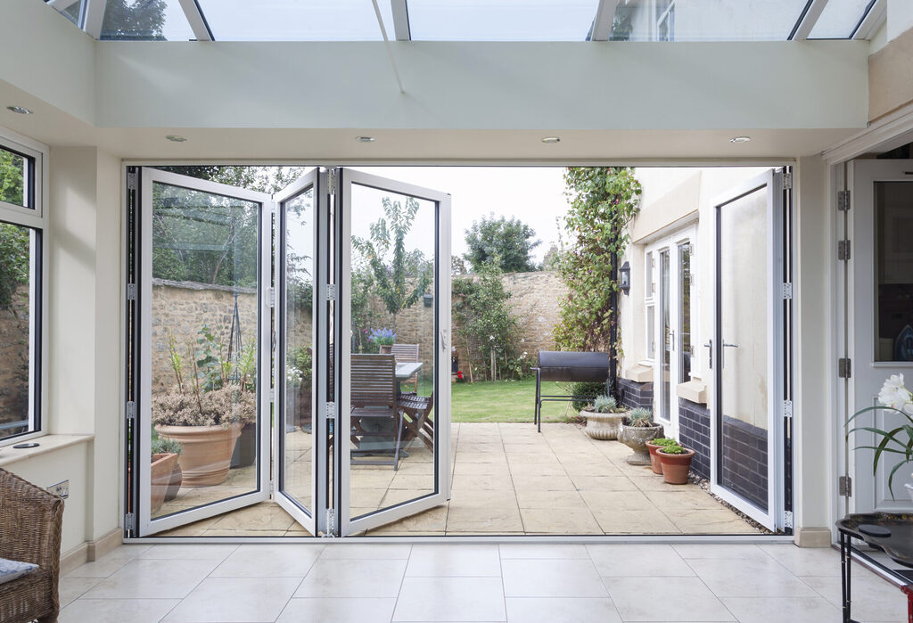 GFD Homes aluminium bifold doors vs upvc : a bifold door semi open looking out onto a patio and garden with a bbq