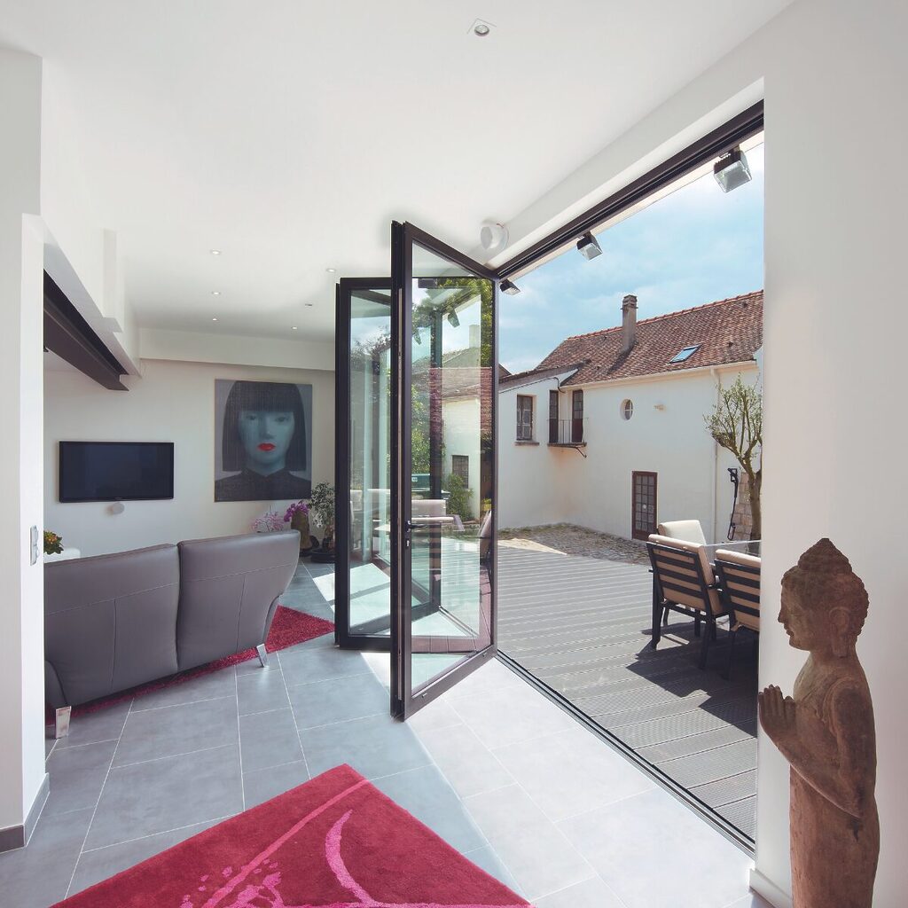 GFD Homes aluminium bifold doors: bifold door half open to allow patio access with sun shining through. 