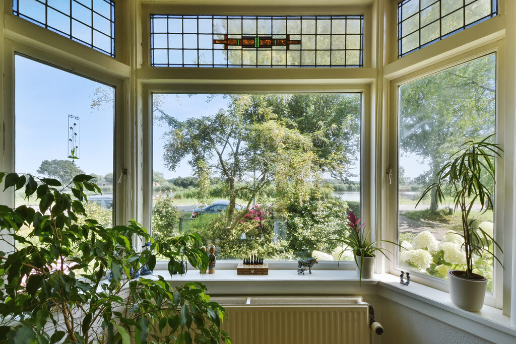 GFD Homes bay window dimensions: looking at a bay window with plant pots around the window and a beautiful garden in show. 